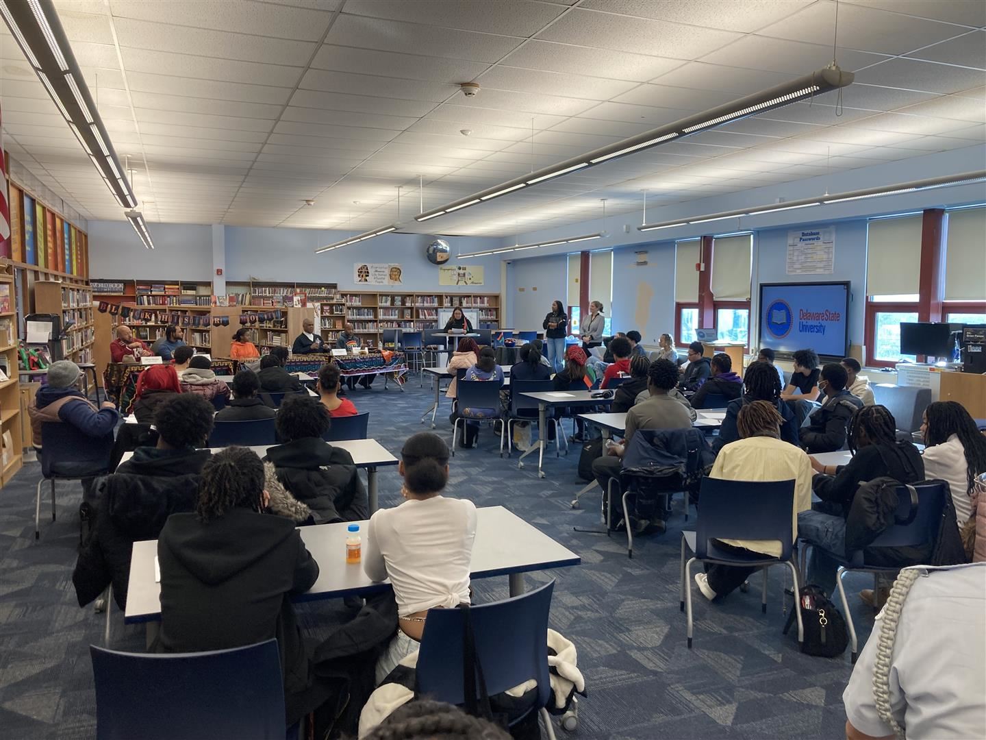 Dozens of students sit at tables listening to a panel