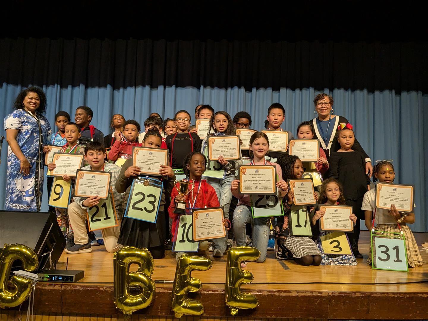  Spelling Bee competitors pose with event coordinators on stage
