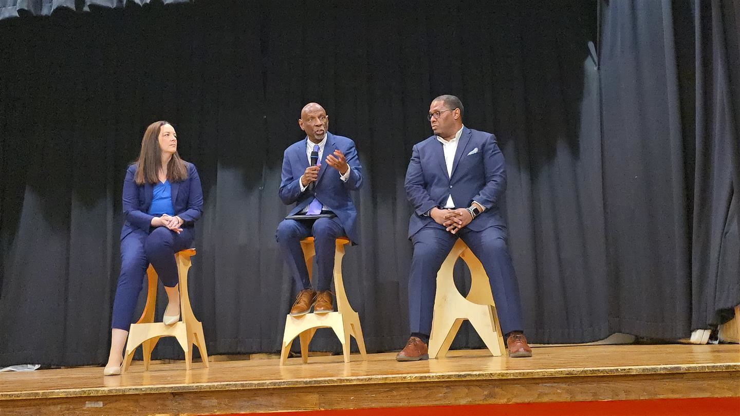  Three people sit on stools on stage