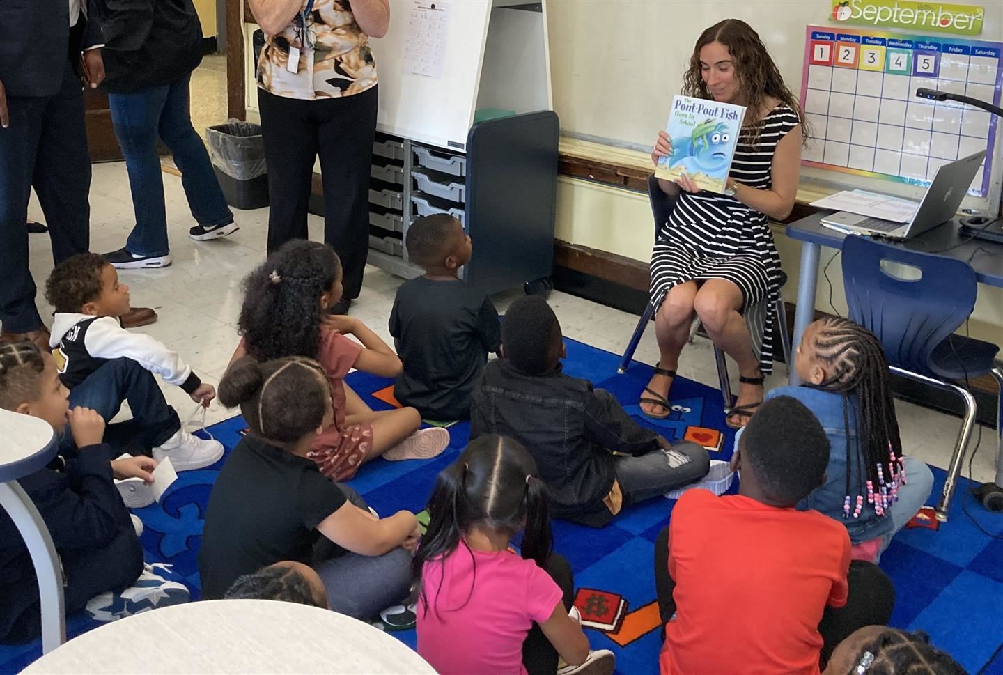 A first grade teacher reads a book to her class