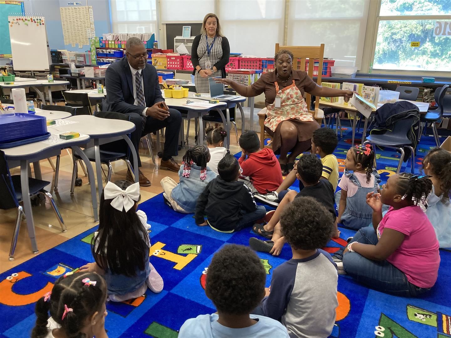 A second grade class speaks with a teacher and superintendent