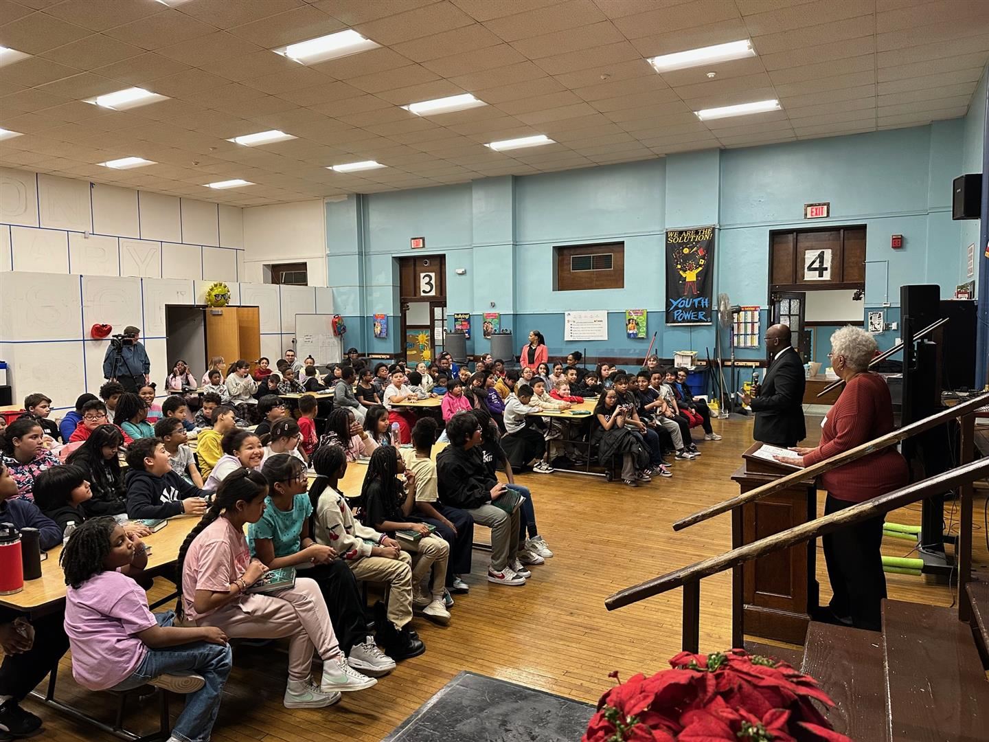 A room full of students listens to a school leader