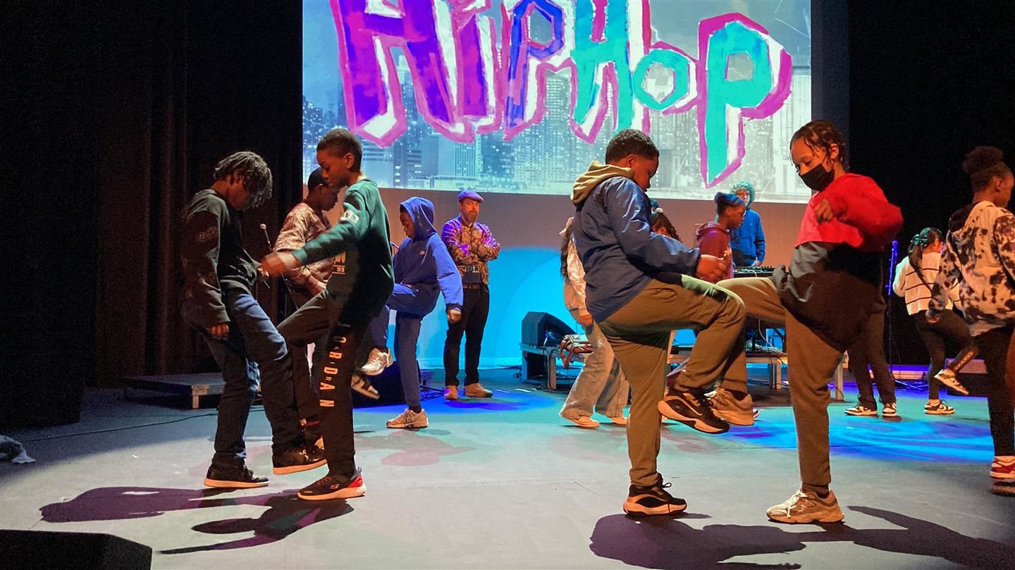  Four students dance on stage as part of a larger group